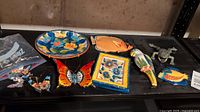 Terracotta and plastic decorative plates, butterfly wall hangings, and cast iron frog doorstop on a black shelf.