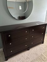 Overall front view of dark stained dresser beneath a round mirror