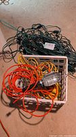 Photo of collection showing multiple green outdoor extension cords and a plastic crate containing orange and yellow cords plus a corded trouble light.