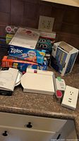 Kitchen counter with assorted boxes of plastic storage bags, tin foil rolls, parchment paper, kitchen scale, slicer, and power outlet extension.