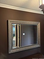 Front view of large ornate rectangular mirror with thick, decorative gold and black frame hung on wall.