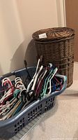 Wicker laundry hamper next to plastic laundry basket filled with assorted plastic clothes hangers.
