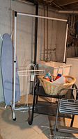 Rolling clothes rack, black rolling cart with basket on top and ironing board in basement laundry area