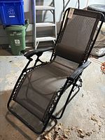 Full view of the outdoor lounger chaise showing the black metal frame, black and beige mesh webbing seat and back, and beige cushion