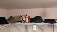 Shelf with various men's hats including fedoras and caps, black umbrella also visible