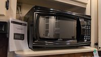 Front view of black Sunbeam microwave showing door, display and control panel on right side, placed on shelf.