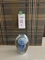 Full view of heavy glass paperweight featuring a blue jellyfish design inside, placed on plaid fabric.