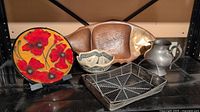 All five items grouped on shelf: poppy plate, wooden fish tray, decorative bowl, pewter pitcher, metal tray