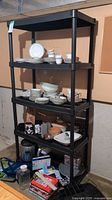Full side view of black plastic shelving unit with multiple shelves containing dishes and kitchenware.