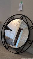 Full view of round wall mirror showing black metal frame with scroll designs and reflection of adjacent room.