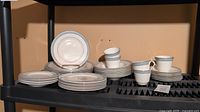 Image showing stacks of various plates and cups with saucers on black shelving, displaying the entire set with the Etude pattern.