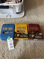 Three Star Trek DVD box sets including The Original Series, The Next Generation First Season, and The Original Series Season 3 arranged side by side on carpet floor.
