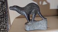 Side view of dark grey carved stone otter on lighter grey stone base, showing full body and tail.