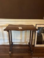 Front view of antique dark wood side table showing ornate spiral legs and scalloped edge table top.
