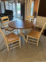 Full set showing round table with cream painted pedestal base and four ladder back chairs with rattan seats arranged around it.
