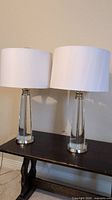 Front view of both lamps side by side on wooden table showing solid glass bases and white drum shades