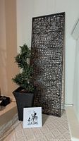 Photo showing faux topiary next to metal wall panel and small tile image propped in front