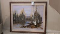 Full view of framed landscape painting showing birch trees by river with mountains in background under brown wooden frame.