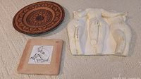 Photo showing three pieces of 3D wall art: ceramic sculpture of three nudes, square tile with nude drawing, terracotta plate with decorative pattern