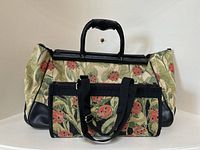 Photo showing the large duffel bag behind the smaller bag, highlighting the ladybug and foliage tapestry pattern and black leather handles with padded grip.