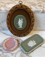 Three vintage Wedgwood Jasperware pieces displayed on marble surface: framed oval plaque, pink round dish, and green rectangular tray