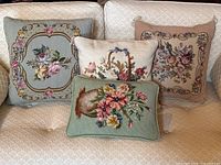 Set of four decorative vintage floral needlepoint pillows arranged on a cream sofa