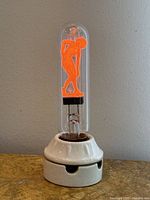 Full frontal view of the Aerolux neon lightbulb showing the orange glowing nude dancer figure mounted on the white porcelain base.