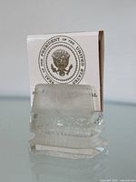 Photo showing the engraved clear crystal matchbook holder with floral and fan motifs, containing the official Presidential matchbook behind it with the Seal of the President of the United States visible.