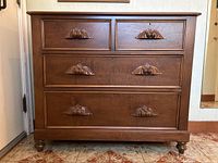 Front view of antique solid wood dresser showing all four drawers with carved moustache handles, standing on bun feet.