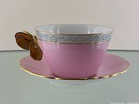Full view of pink teacup with gold butterfly handle on pink saucer showing detailing and condition