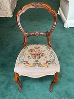 Front view of antique Victorian wooden chair with carved balloon back and needlepoint seat upholstery featuring floral design.