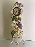 Full view of porcelain mantle clock with detailed floral motifs and ornate base.