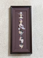 Full view of vertically framed porcelain half pin cushion dolls arranged in shadow box