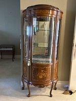 Full front view of bow front cabinet showing glass door, floral inlay and carved legs