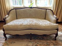 Full front view of loveseat showing carved wood frame and cream damask upholstery