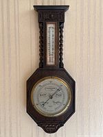 Full view of antique oak wall barometer and thermometer mounted on wall, showing overall size and design