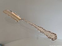 Full view of the cheese scoop showing the ornate handle and scoop blade.