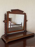 Front angle of antique walnut vanity mirror showing the bobbin-turned side supports and carved top detail with clear reflective glass.