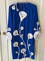 Front view of electric blue dress with white calla lily appliqués hanging on hanger