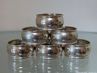 Six napkin rings arranged in a pyramid formation on reflective surface, front view.