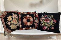 Three front-facing needlepoint pillow designs on a display shelf with a black velvet pillow behind