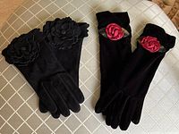 Two pairs of gloves laid flat showing one pair with black leather and floral appliques, the other with black velvet and red rose appliques.