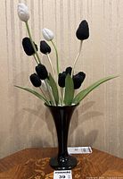Full view of arrangement showing black and white tulip buds, green leaves, white sand, and black vase.