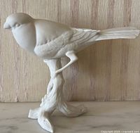 Front view of white porcelain bird perched on twig base against striped background