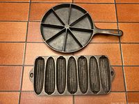 Photo showing top view of both cornbread skillets on a tiled surface: round skillet with 8 wedge sections and rectangular pan with 7 corn cob molds.