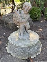 Front view of cast concrete cherub holding a fish atop circular basket-weave base