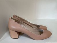 Side profile of both pumps on tabletop showing block heel and scalloped trim