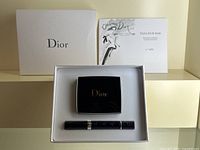 White textured Dior gift box open showing foam insert with black compact, black tube lip colour and certificate card