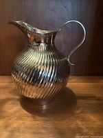 Front view of the silver plated water pitcher showing the fluted body, large handle, and wide spout.