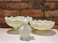 Front angle view of three custard uranium glass pieces, two bowls and one vase, showing pale yellow matte finish and detailing